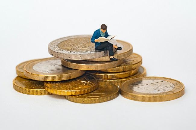 une personne lit un journal sur une pile de pièces de monnaie