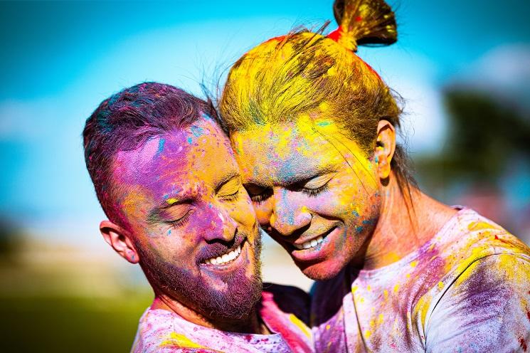 Deux hommes souriant dans les bras l'un de l'autre, recouverts de peinture multicolore