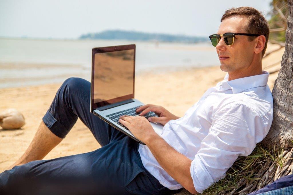 homme qui investit en SCPI depuis son ordinateur sur la plage 