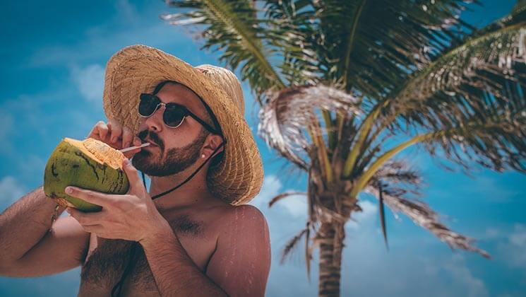 un homme déguste une noix de coco sous les palmiers