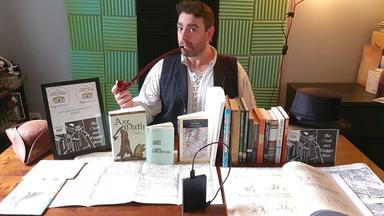 Cary Graham pose à son bureau, avec une pipe et de nombreux livres et documents