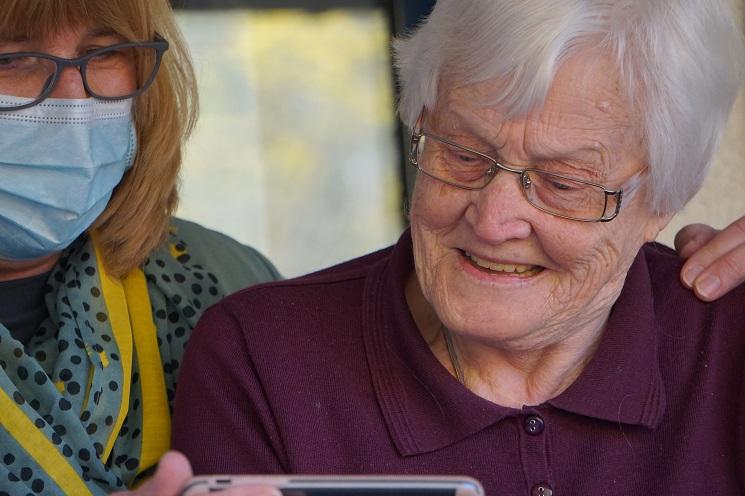 une personne âgée accompagnée d'une femme avec un masque hygiénique consulte l'écran d'un téléphone portable