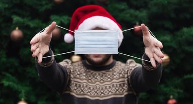 Un homme portant un chapeau de pere noel avec un masque devant le visage.