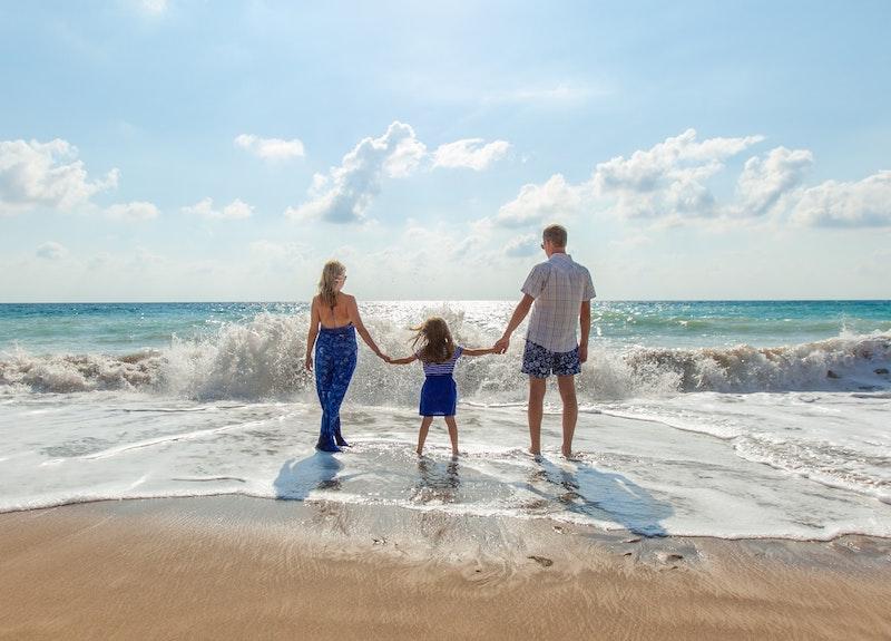 Une femme un enfant et homme qui se tiennent par la main et marchent vers la mer