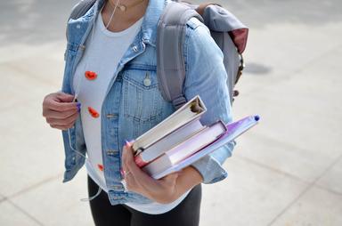 Une personne avec une veste en jean bleu, un cartable et des documents dans sa main