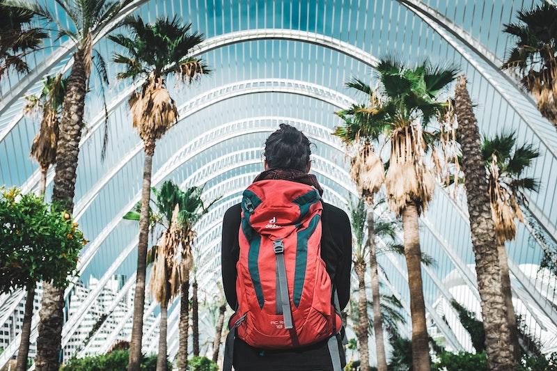 une personne de dos avec un sac a dos rouge au milieu des palmiers a valencia