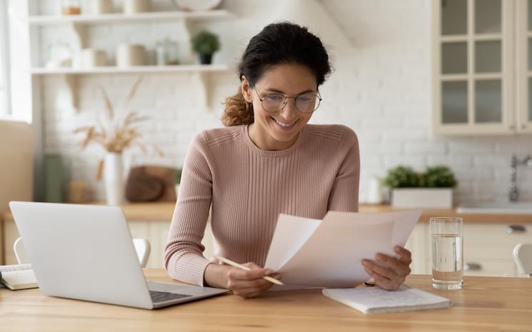 Femme souriante avec ordinateur lisant un papier  