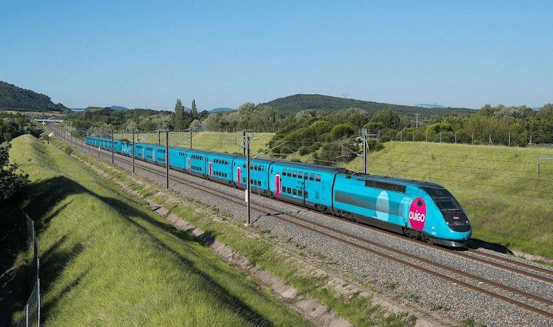 un train bleu ouigo en train de rouler sur des rails