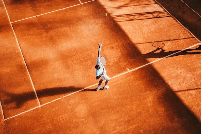 un tennisman en train de servir sur un terrain de terre battue 