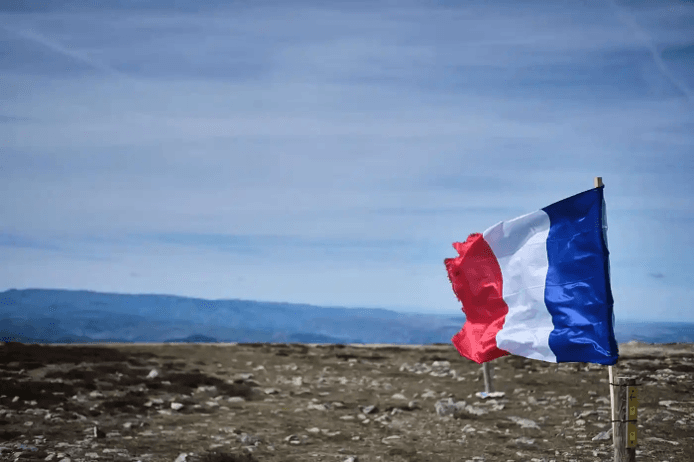 Un drapeau français flotte en haute d'une montagne sous un ciel bleu 