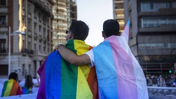 Un homme avec un bras sur l'épaule d'un autre et des drapeaux LGTBI à Valencia