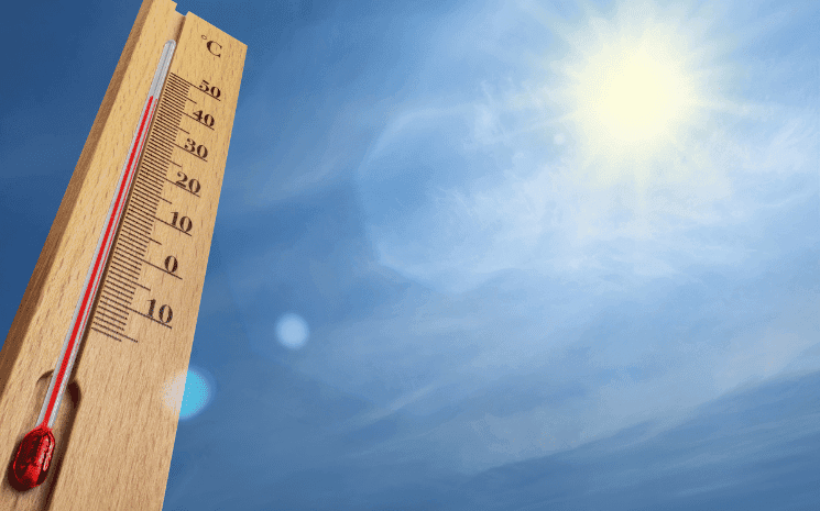 Un thermomètre avec un ciel bleu et un grand soleil derrière