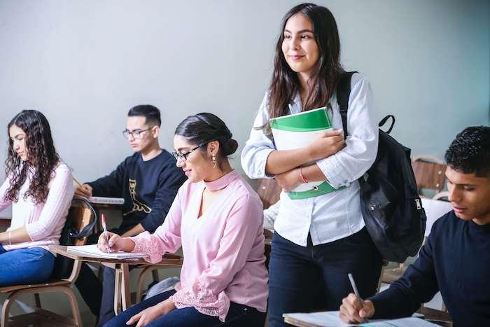 une élève tenant des livres dans sa main aux côtés de ses camarades dans une classe d'école