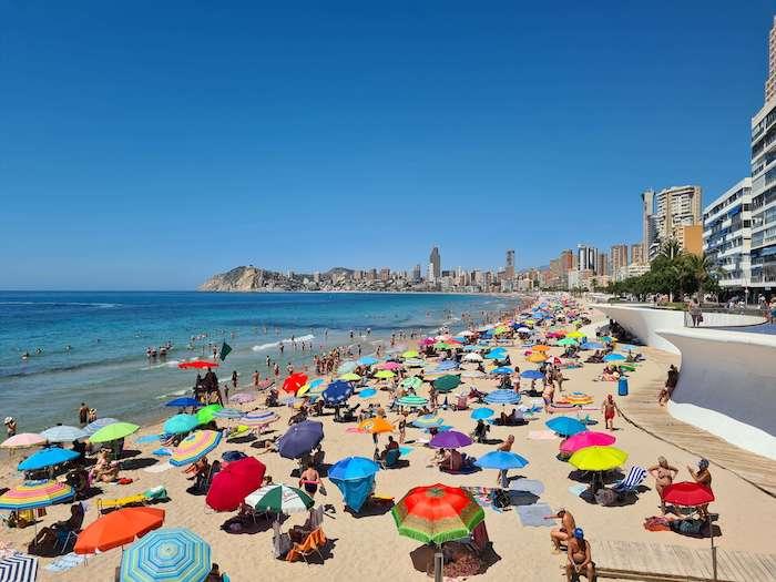 des touristes avec des parasols sur une plage de Benidorm dans la Communauté valencienne