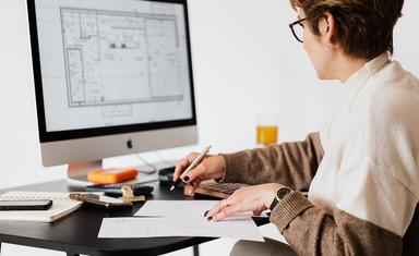 femme assise au bureau écrit sur une feuille devant écran d'ordinateur