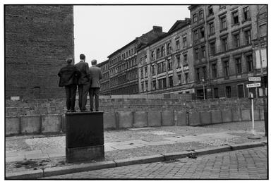 Une photo de Henri Cartier Bresson montrant trois hommes en train de regarder au dessus du mur de Berlin