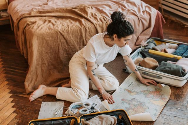 Jeune femme préparant son voyage, carte à la main et valise ouverte à ses côtés, dans une ambiance cosy