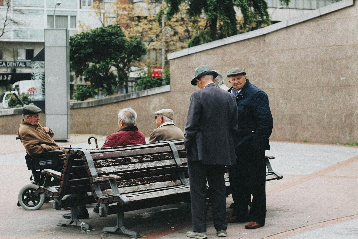 Groupe de personnes âgées assises sur un banc dans un parc avec un homme debout regardant vers l'objectif