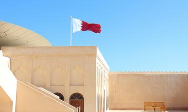 Drapeau du Qatar flottant, ciel bleu et batiment Qatari