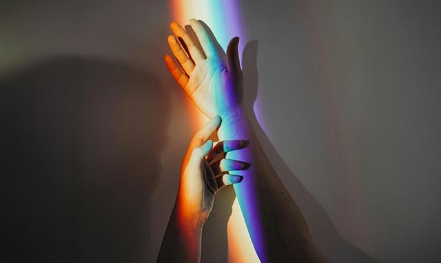 Deux mains se touchent intimement sous une lumière arc en ciel
