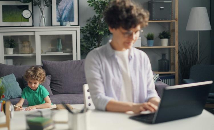 Une femme assise devant son ordinateur avec son enfant derrière