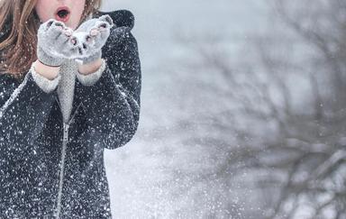 femme avec veste a capuche zippee noire soufflant sur de la neige