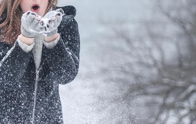 femme avec veste a capuche zippee noire soufflant sur de la neige