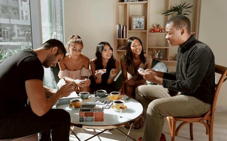 Un groupe de cinq personnes discutent et rient assis autour d'une table en buvant un café