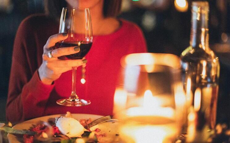 Femme qui tient un verre de vin rouge dans la main dans un restaurant devant une assiette