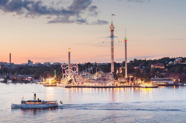 Parc d'attractions éclairé au bord de l'eau avec un bateau qui passe au coucher de soleil