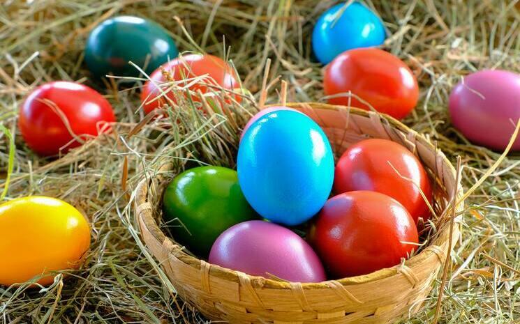 Plusieurs œufs peint en bleu, rouge, rose, vert et jaune dans un panier