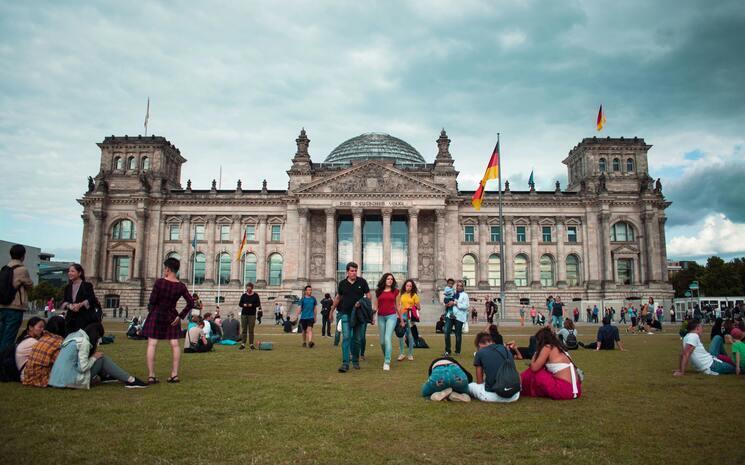 plusieurs personnes assisent dans l'herbe face au Reichstag à Berlin