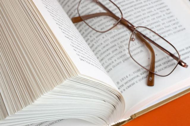 Un livre ouvert situé sur une table, une paire de lunettes posée sur la page droite.