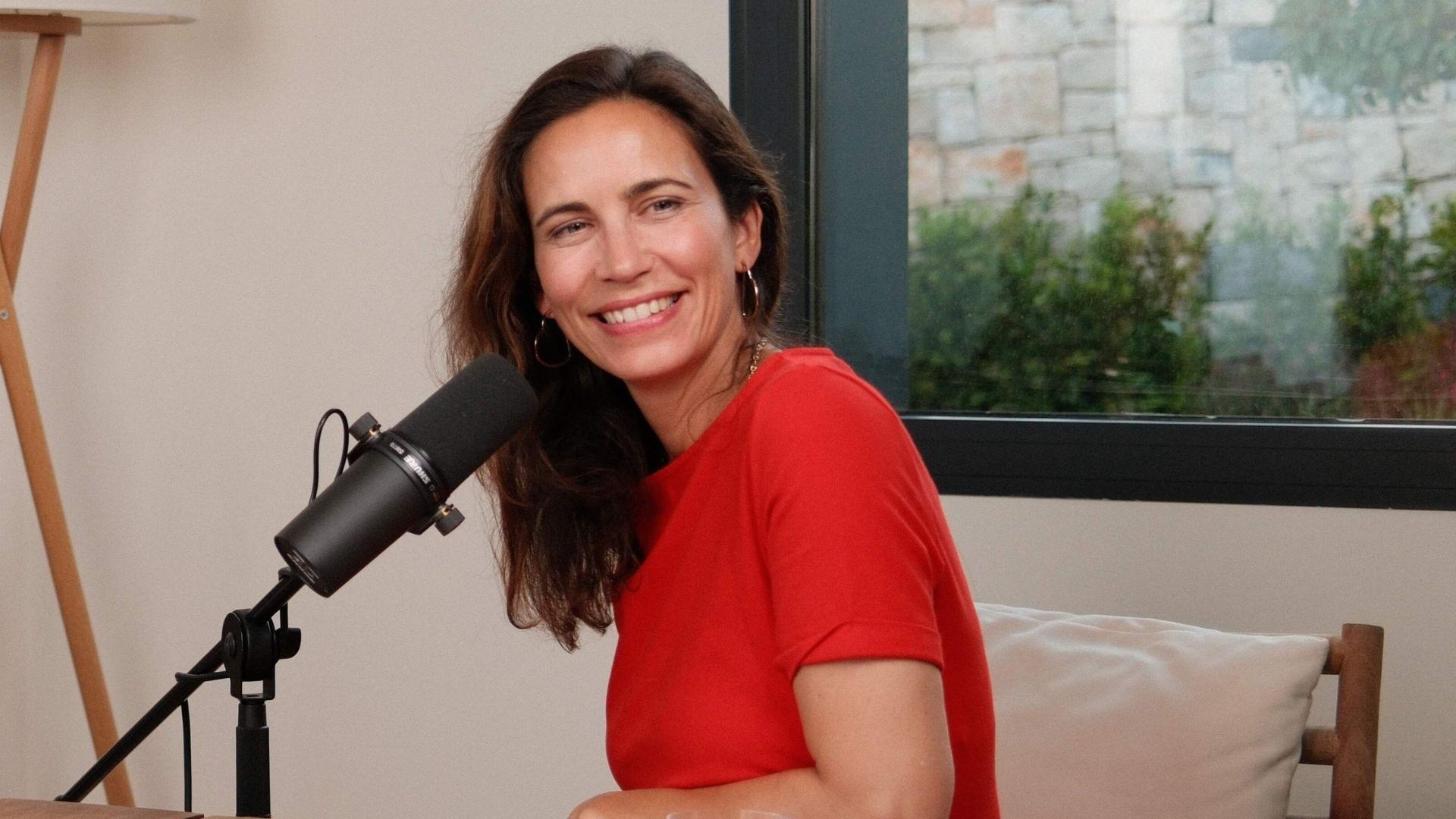 une femme avec un haut rouge sourit devant un micro