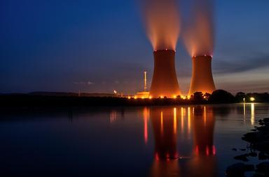 Vue de deux tours de refroidissement nucléaire au crépuscule, de l'autre côté d'un fleuve