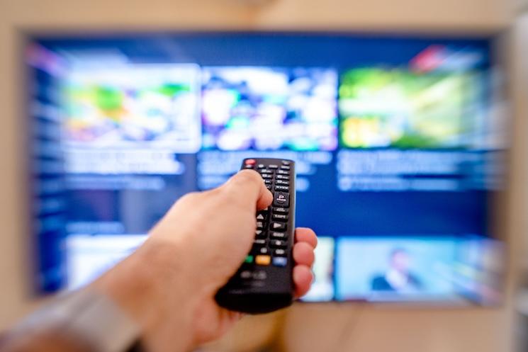 Une main qui change de chaîne à l'aide d'une telecommande en face des plusieurs écrans