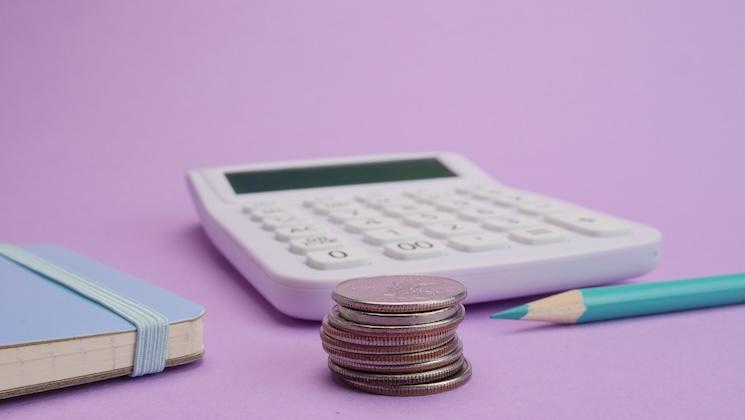 Une calculette avec des pieces et un crayon sur un fond mauve