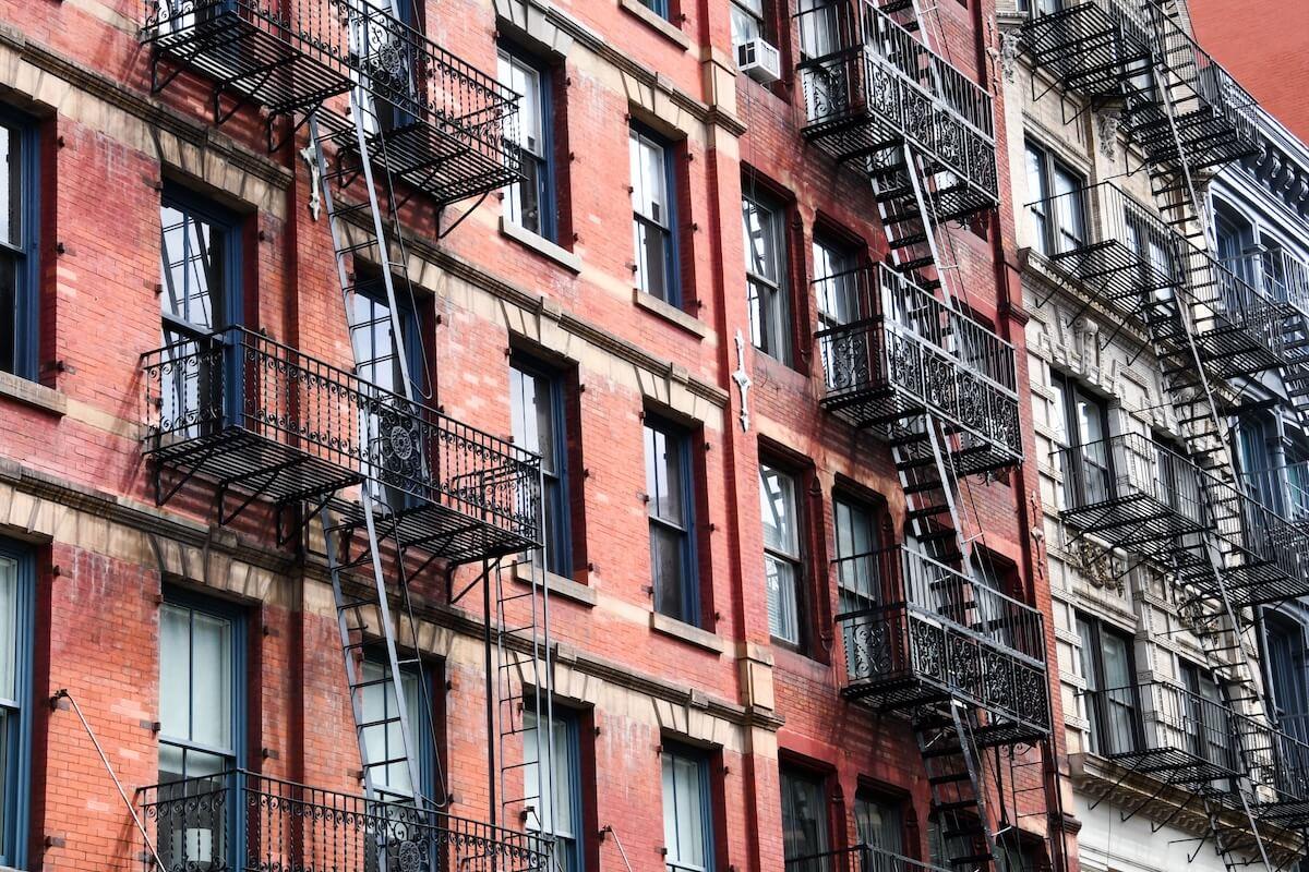 Façade d'un immeuble en briques à New York avec ses emblématiques escaliers de secours en métal noir, sur fond de ciel urbain