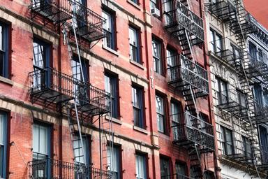 Façade d'un immeuble en briques à New York avec ses emblématiques escaliers de secours en métal noir, sur fond de ciel urbain