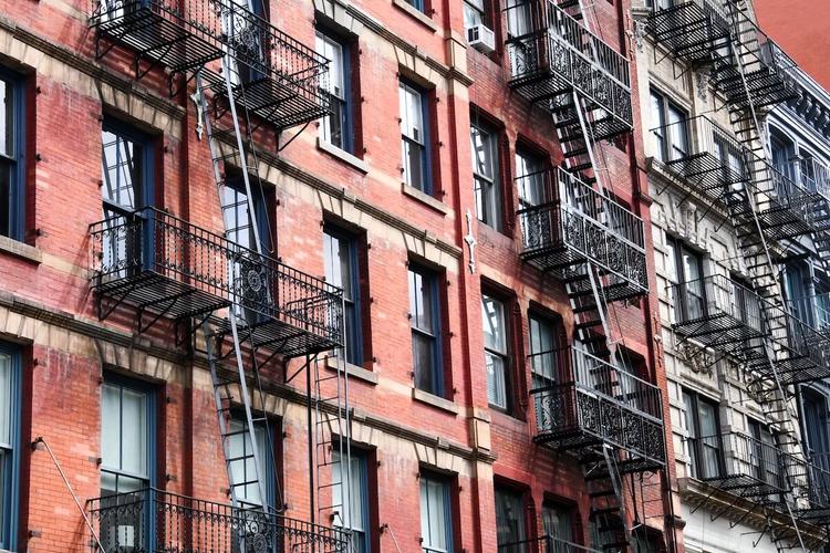 Façade d'un immeuble en briques à New York avec ses emblématiques escaliers de secours en métal noir, sur fond de ciel urbain