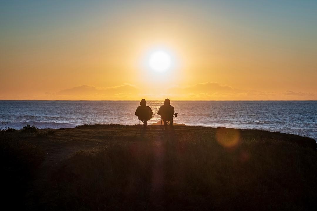 Deux personnes assises face à la mer au coucher du soleil.