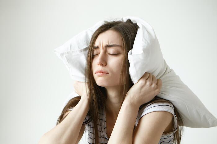  jolie femme étudiante en t-shirt rayé essayant de dormir, assise avec un oreiller 