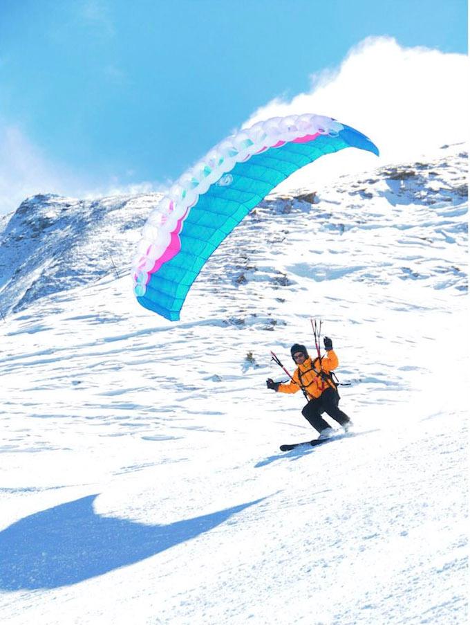 une personne descend avec ses skis et un parapente