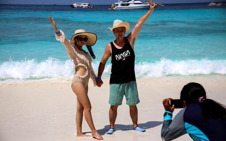 Un couple de touristes chinois salue la camera sur une plage de Thailande