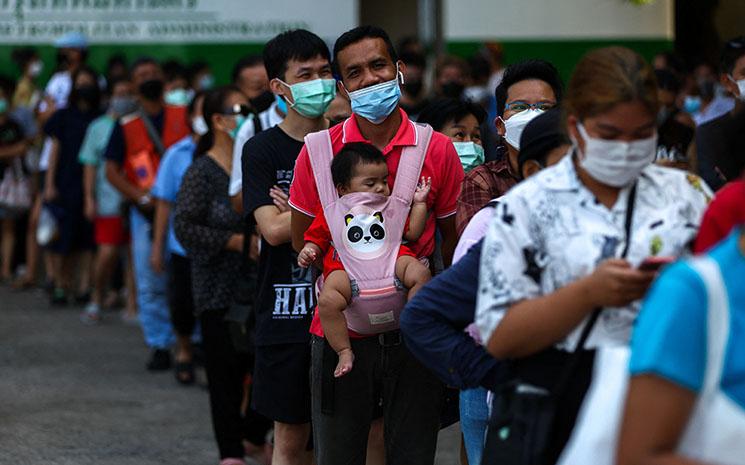 Un pere de famille fait la queue pour voter en Thailande en portant son bebe