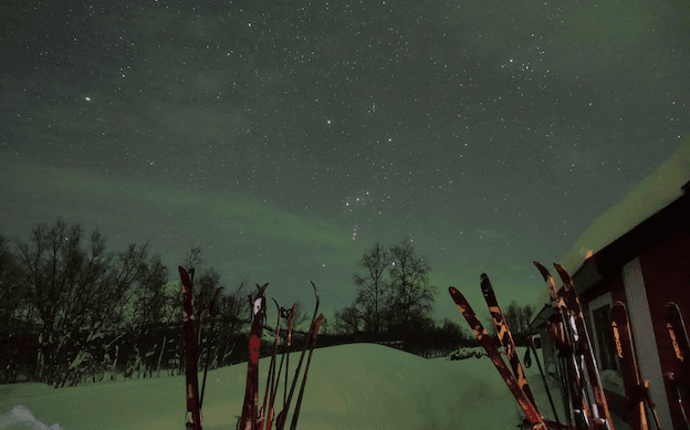 Des aurores boréales : en premier plan des skis, et des étoiles dans le ciel