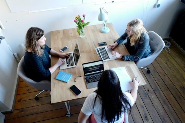 trois employées assises, discutant ensemble autour d'un bureau