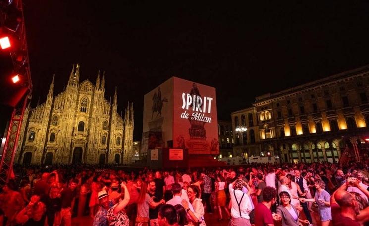 des gens dansent sur une place la nuit devant la cathédrale de milan éclairée