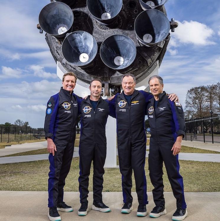 quatre astronautes en tenue bleue devant un réacteur de fusée  