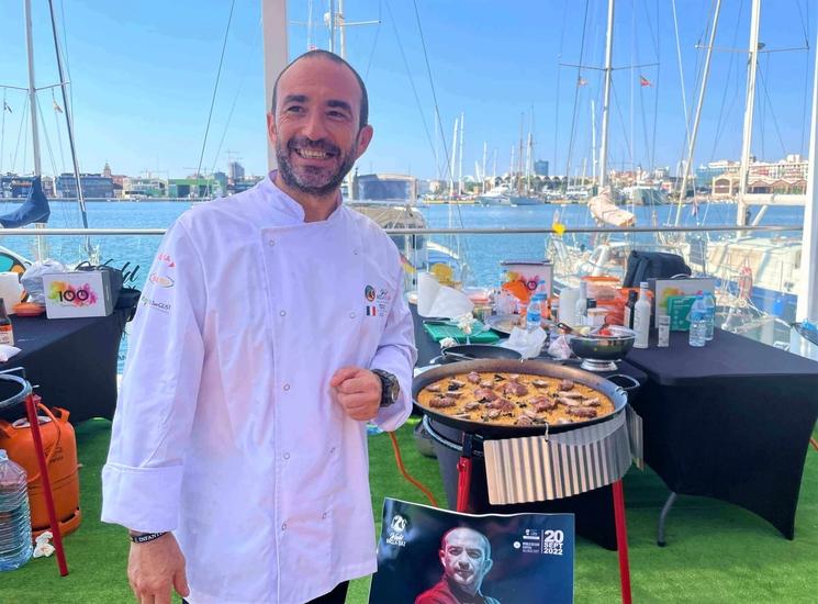 eric gil en tenue blanche de cuisiner devant une paella